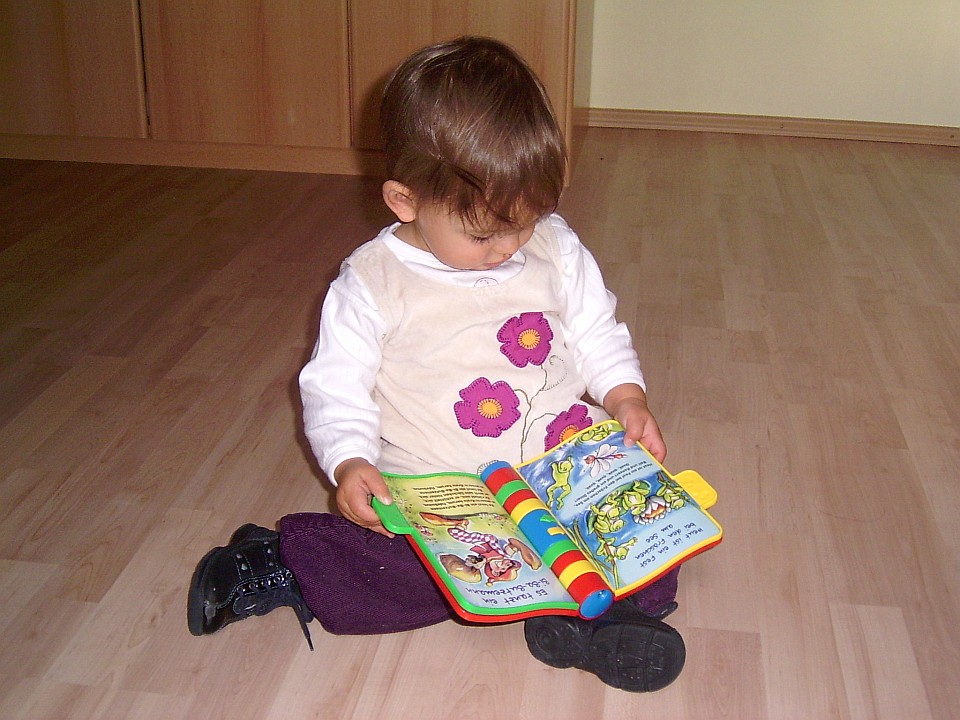 Kleinkind sitzt auf dem Fußboden mit einem Lern- und Spielbuch