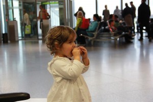 Kleines Mädchen mit Brötchen im Mund im Wartesaal auf dem Flughafen